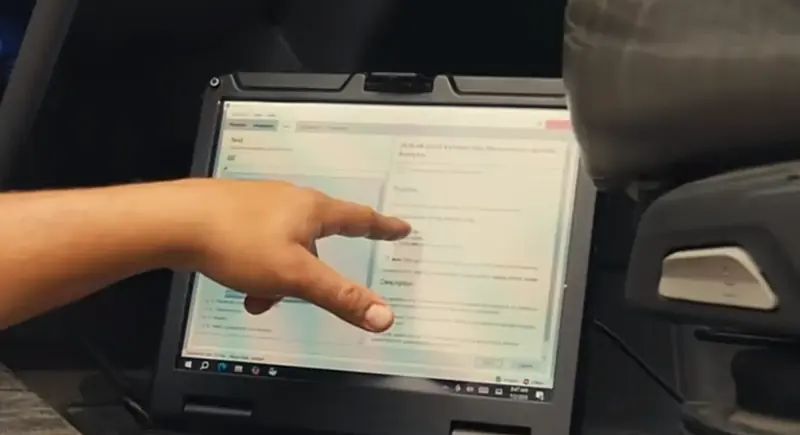 A hand pointing at a software window on a rugged laptop inside a truck cab