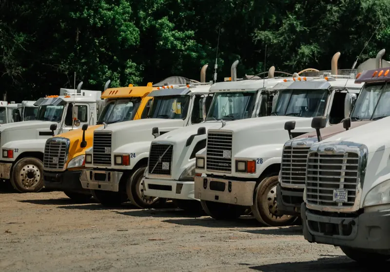 A row of parked white and yellow semi trucks on a gravel lot